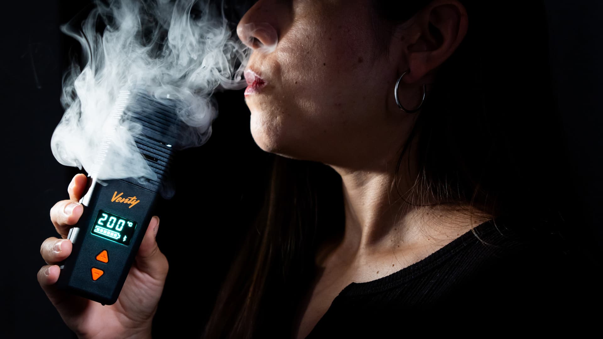 A dense cloud of visible vapor exhaled from a portable vaporizer against a dark backdrop