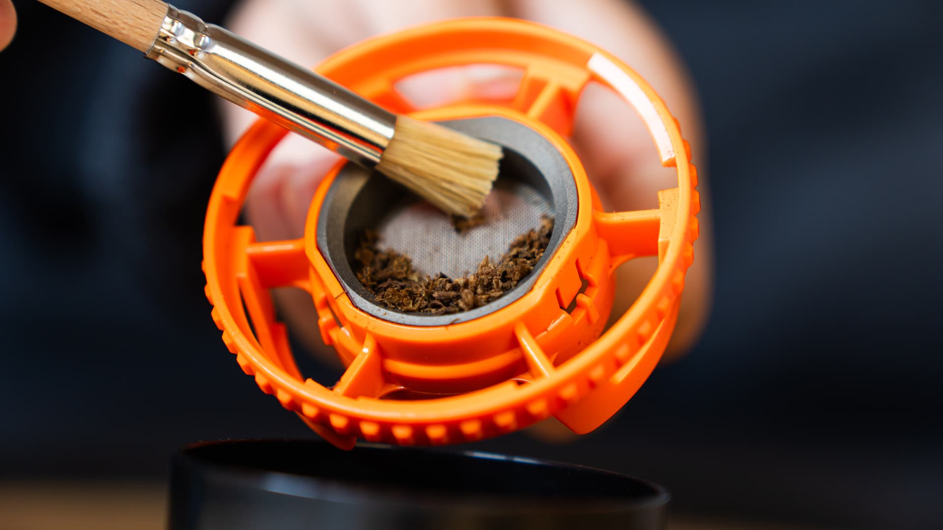 Verbrauchtes Cannabis wird aus der Füllkammer mit orangem Rahmen gebürstet