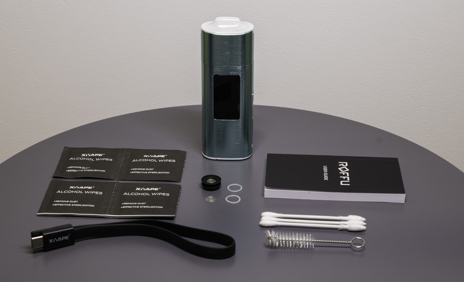 XLUX Roffu teal vaporizer complete unboxing kit with USB-C cable, cleaning brushes, alcohol wipes, and user guide on dark table