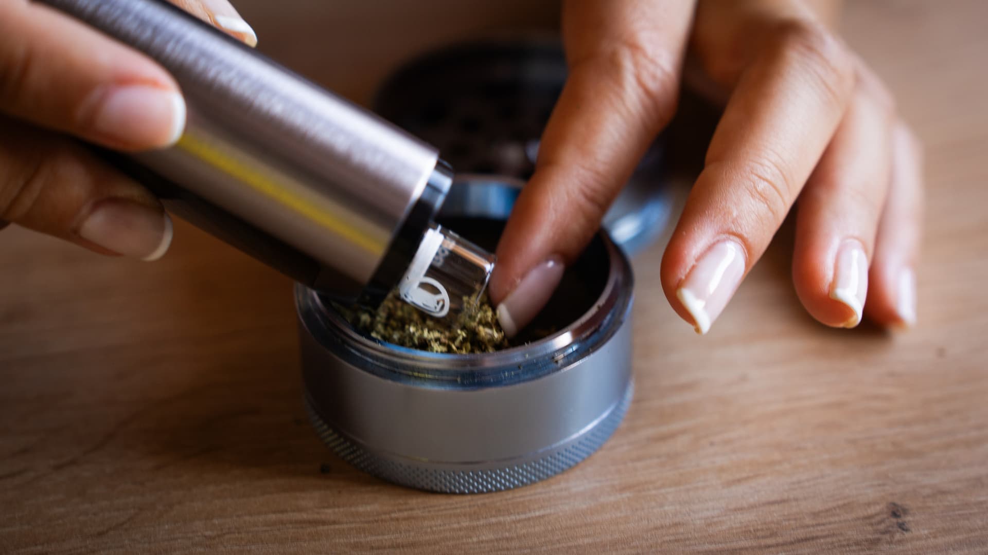Close-up of XLUX Roffu glass chamber being loaded with herb from a metal grinder on wooden table