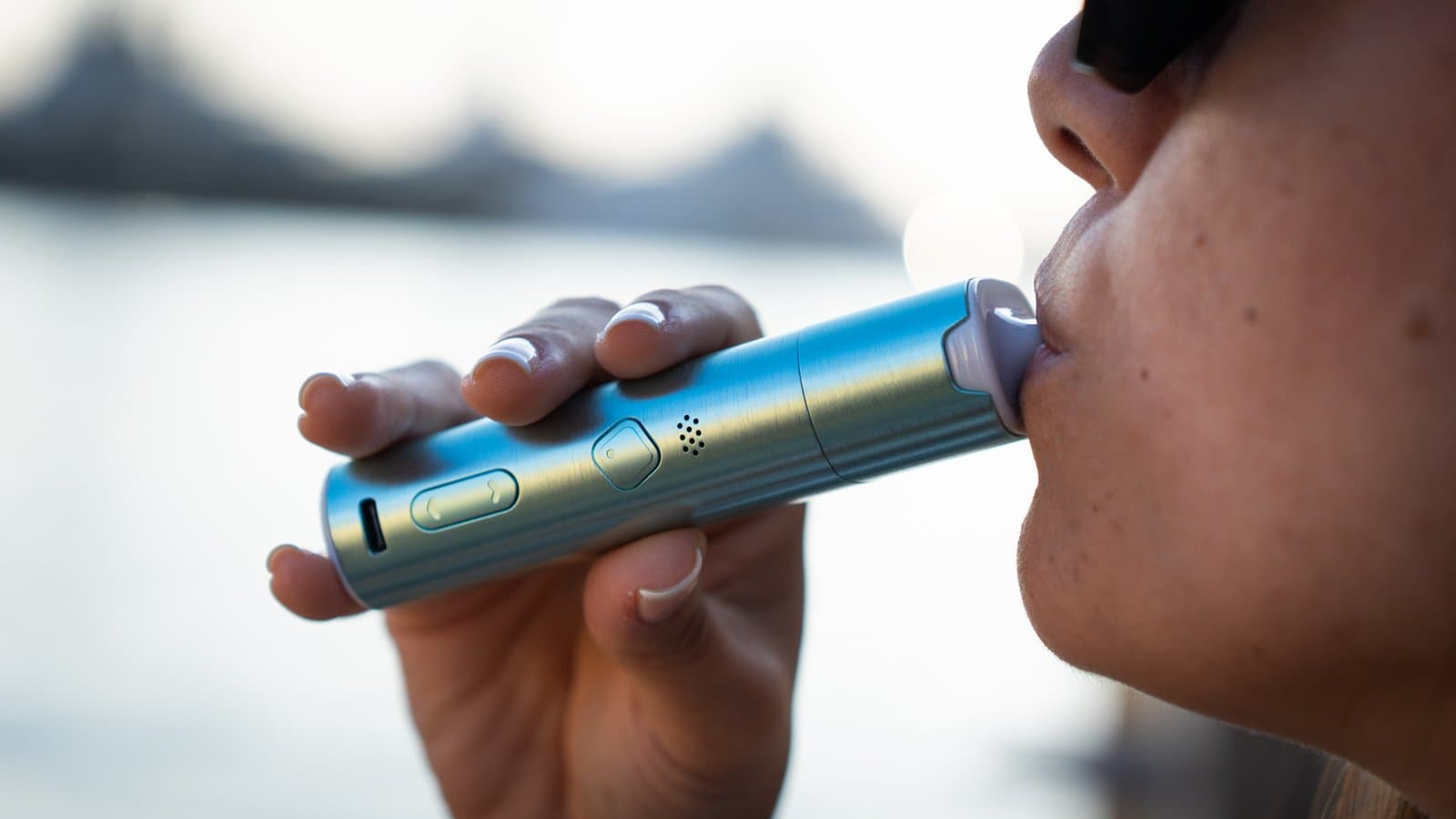 Person zieht im Freien am Wasser zur goldenen Stunde am türkisfarbenen XLUX Roffu, seitliche Bedienelemente und USB-C-Anschluss sichtbar