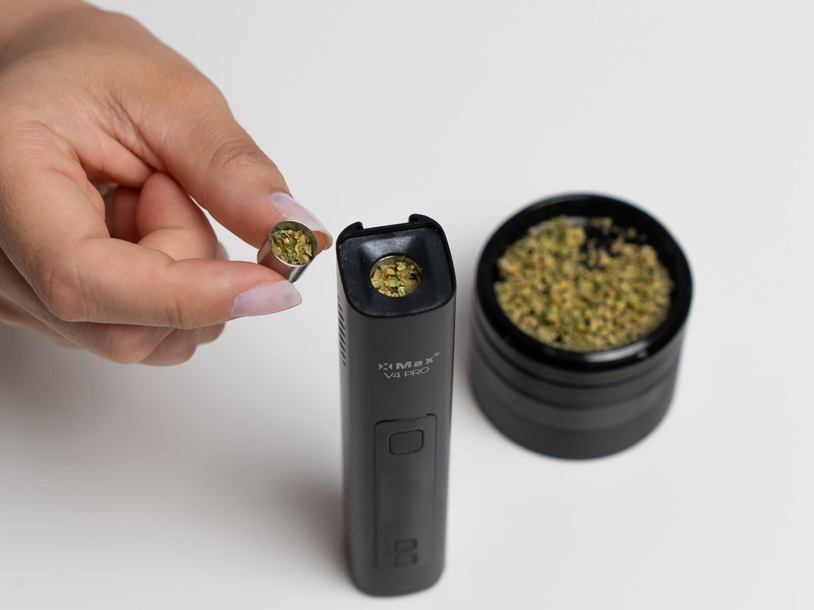 Heizkammer des XMax V4 Pro mit gemahlenem Cannabis befüllt, daneben eine gefüllte Dosierkapsel und ein Grinder im Hintergrund