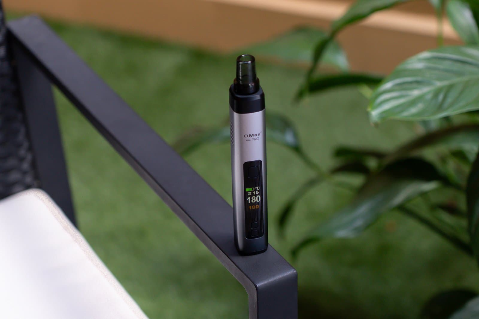 XMax V4 Pro auf der Armlehne eines Gartenstuhls, das OLED-Display zeigt 180°C, grüne Pflanzen im Hintergrund