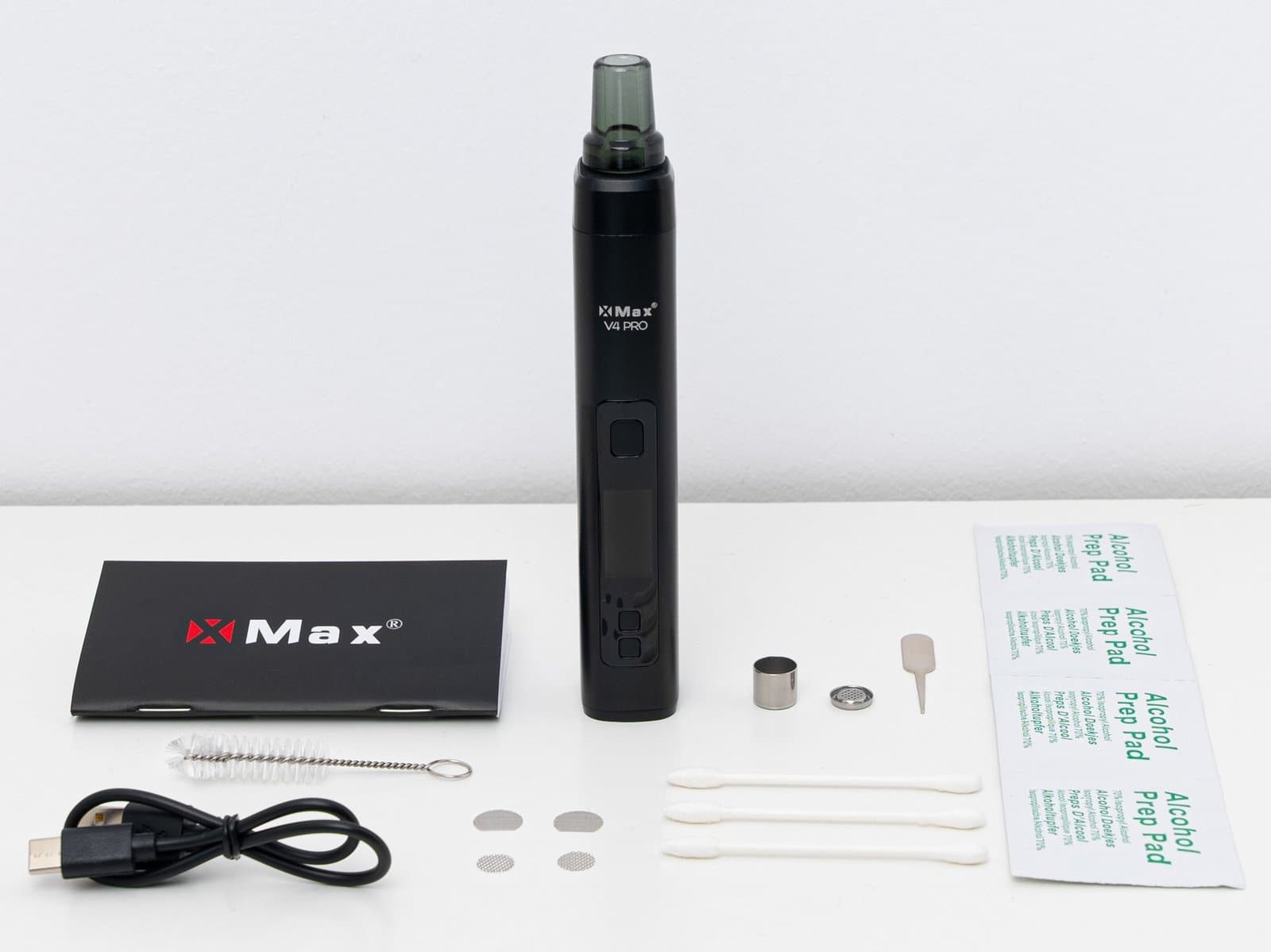 XMax V4 Pro Unboxing-Flatlay mit dem Vaporizer, USB-C-Kabel, Edelstahl-Dosierkapsel, Reinigungsbürste, Ersatzsieben, Stopfwerkzeug und Bedienungsanleitung