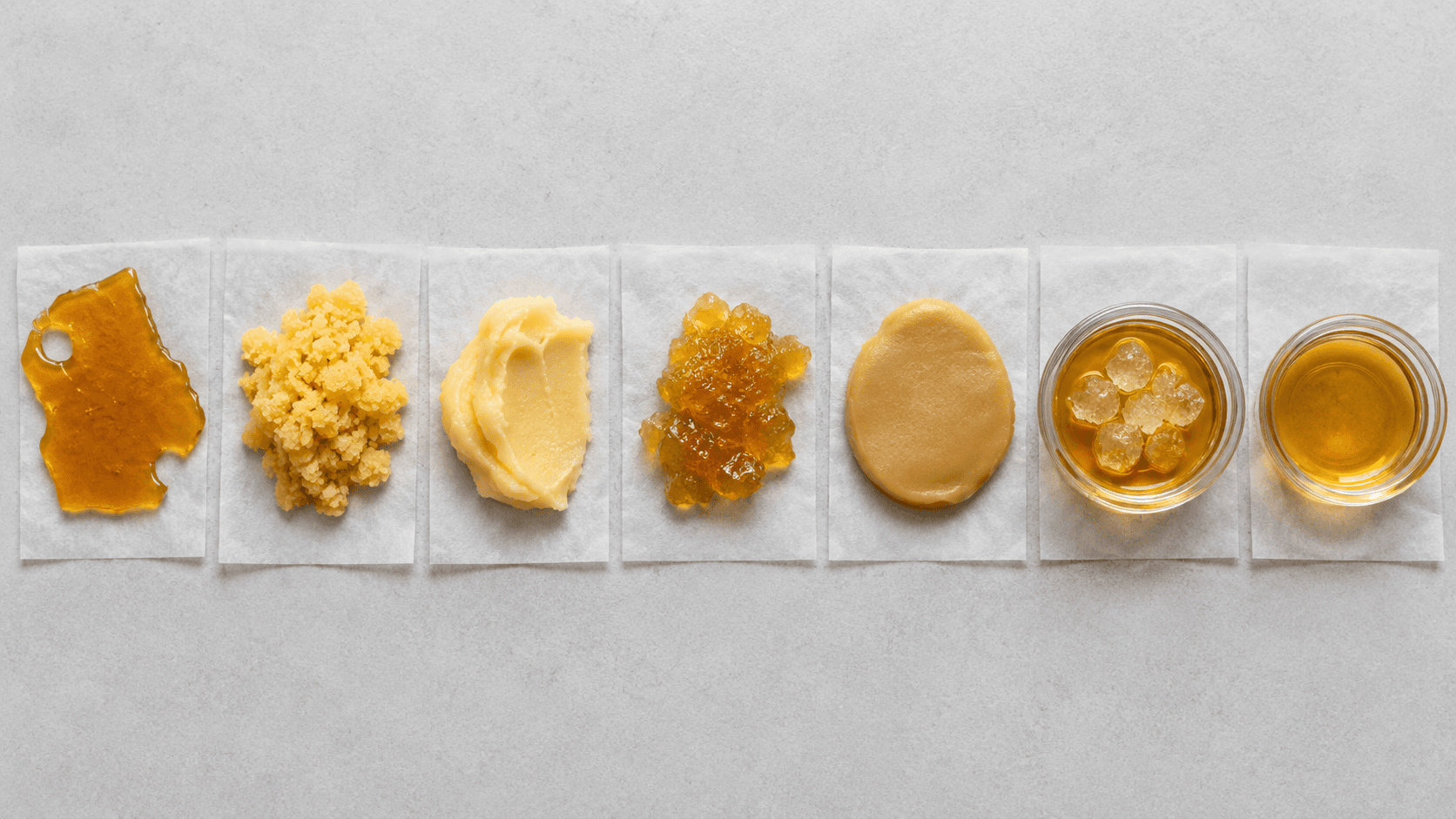 Flat-lay of seven different cannabis concentrate textures arranged in small glass containers and on parchment squares
