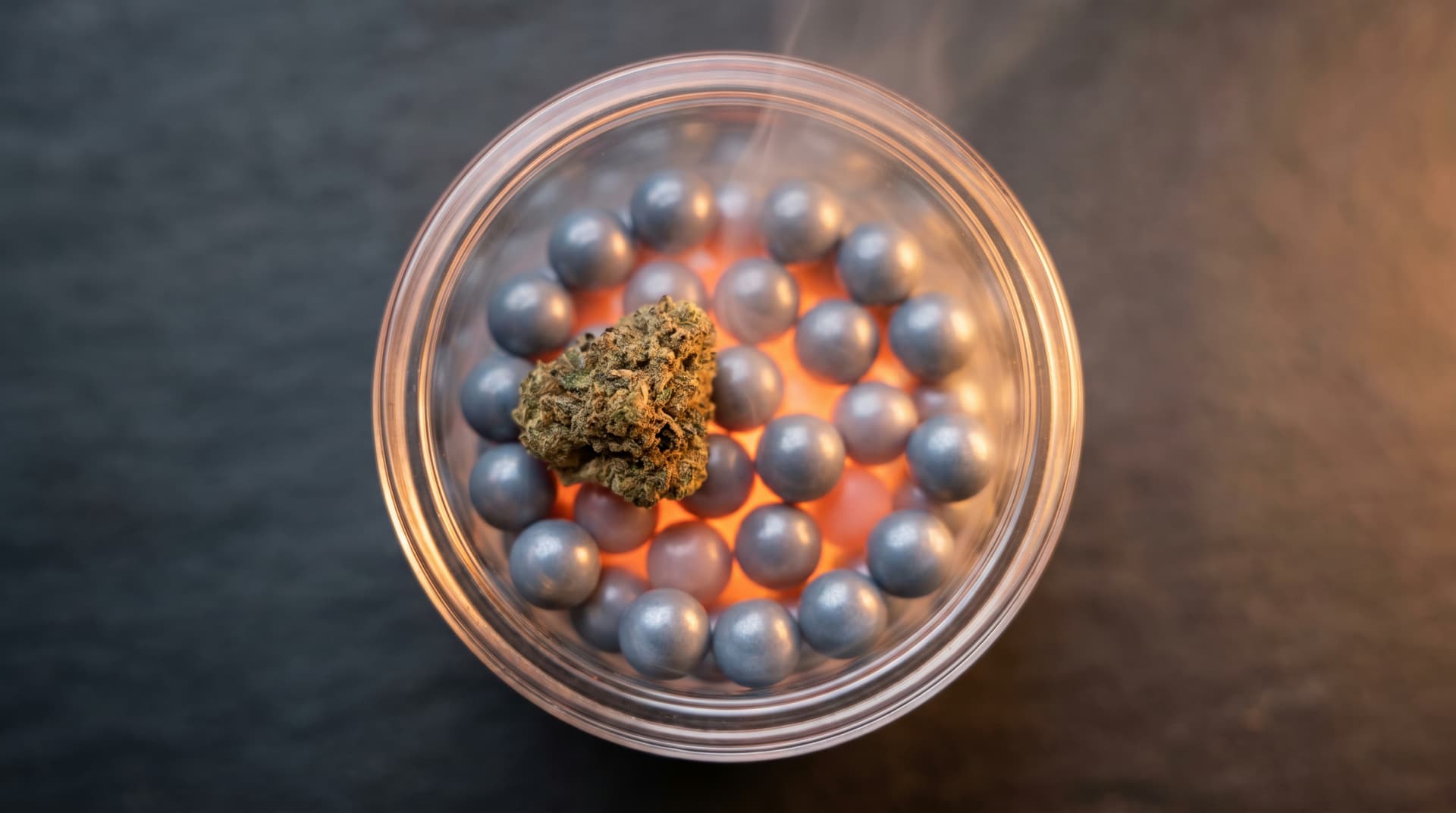 Macro top-down view of a quartz chamber filled with glowing silicon carbide balls and a single nugget of ground cannabis resting on top
