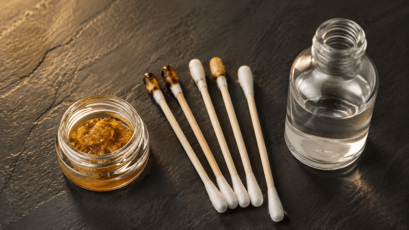 Cotton swabs, isopropyl alcohol, and a jar of concentrate on dark slate