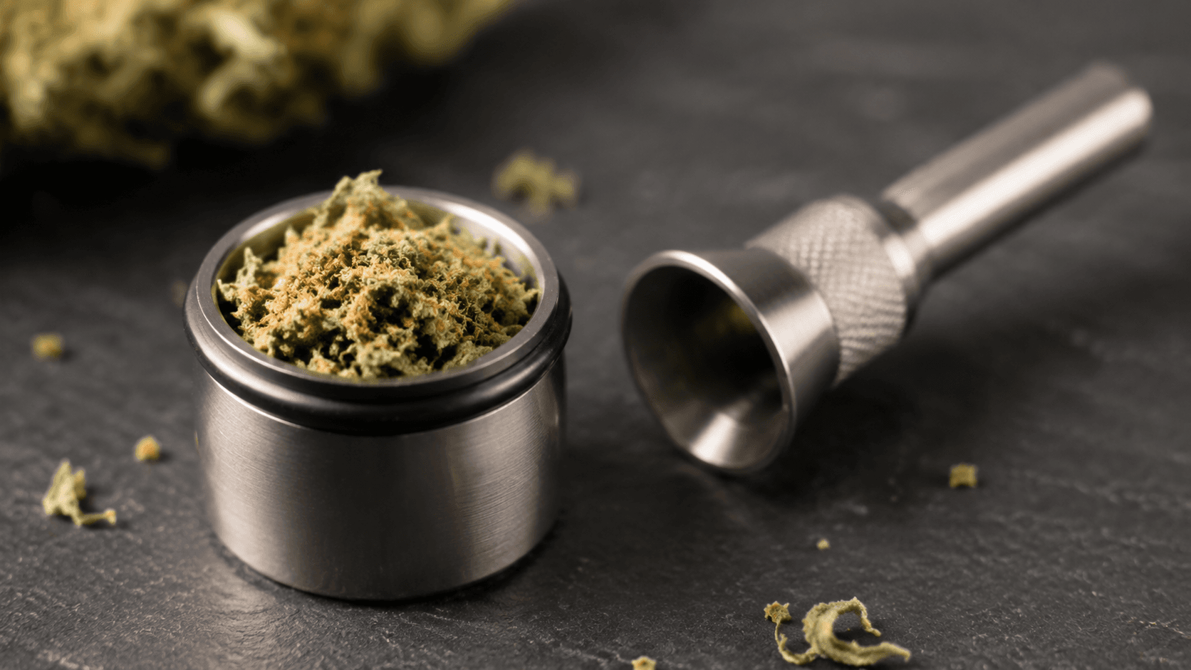 Stainless steel vaporizer bowl loosely filled with fluffy ground cannabis next to a metal loading funnel on a dark slate surface