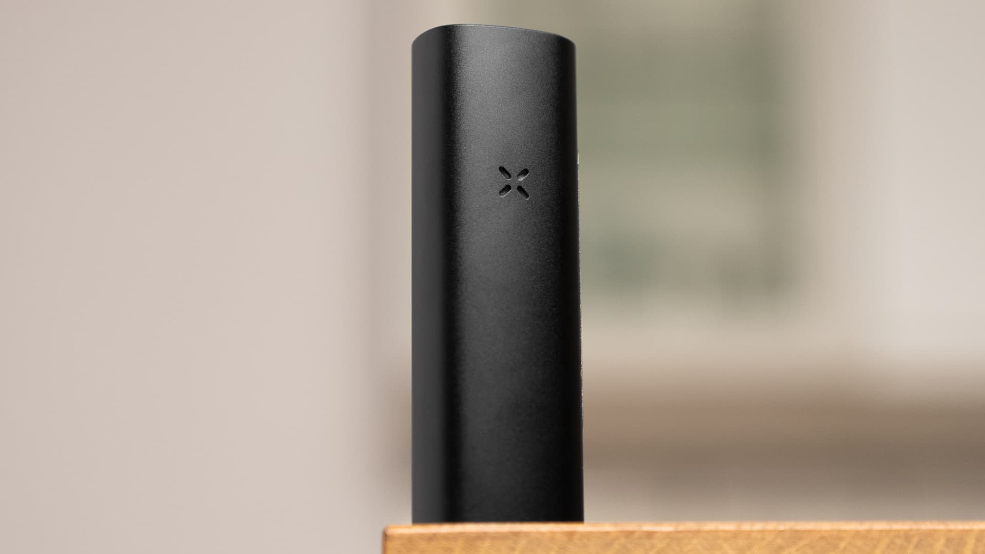 PAX Mini 2 session conduction vaporizer standing on a wooden shelf with warm bokeh background