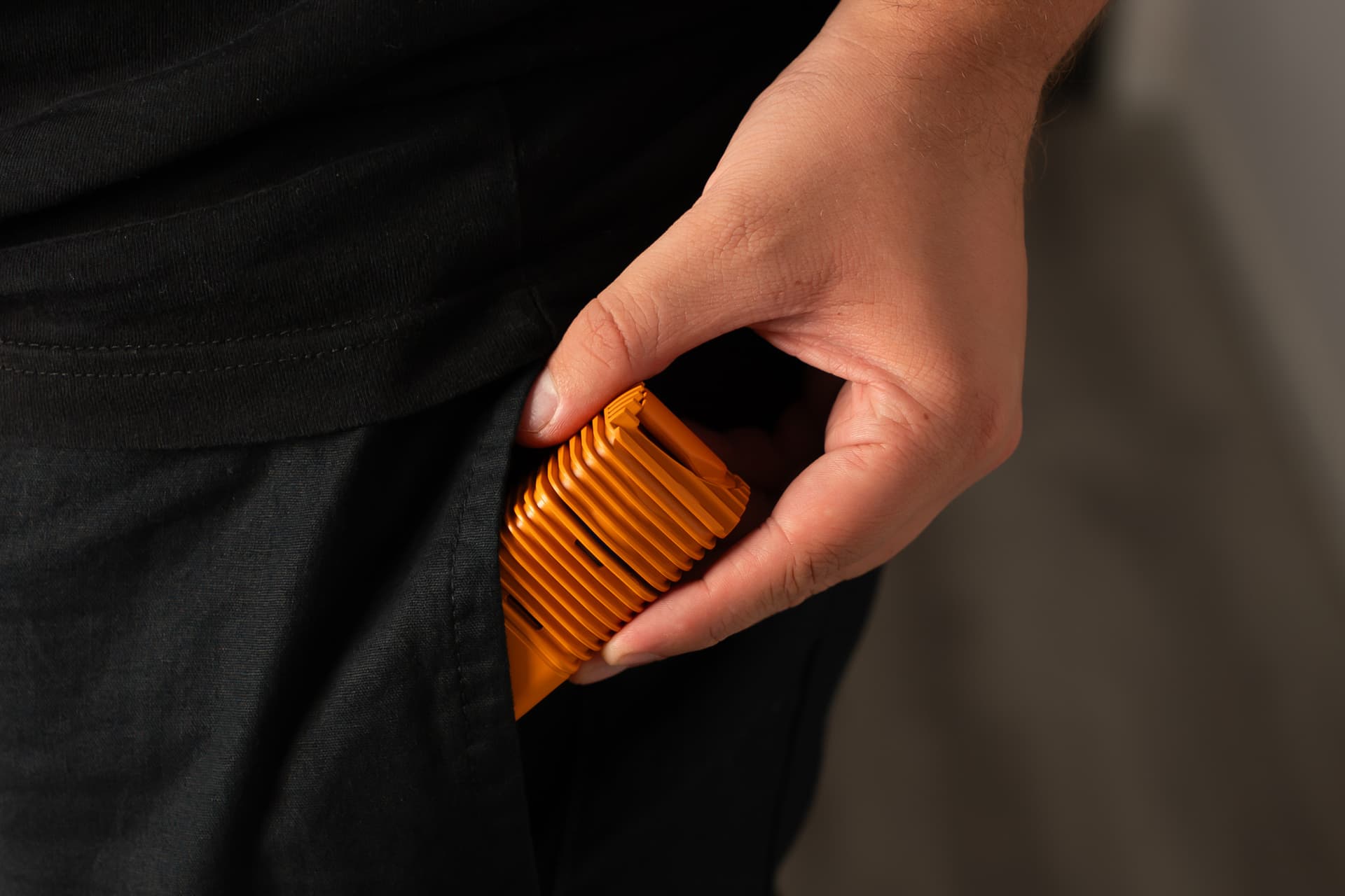 Hand sliding an orange Veazy vaporizer into a trouser pocket showing its compact pocketable size