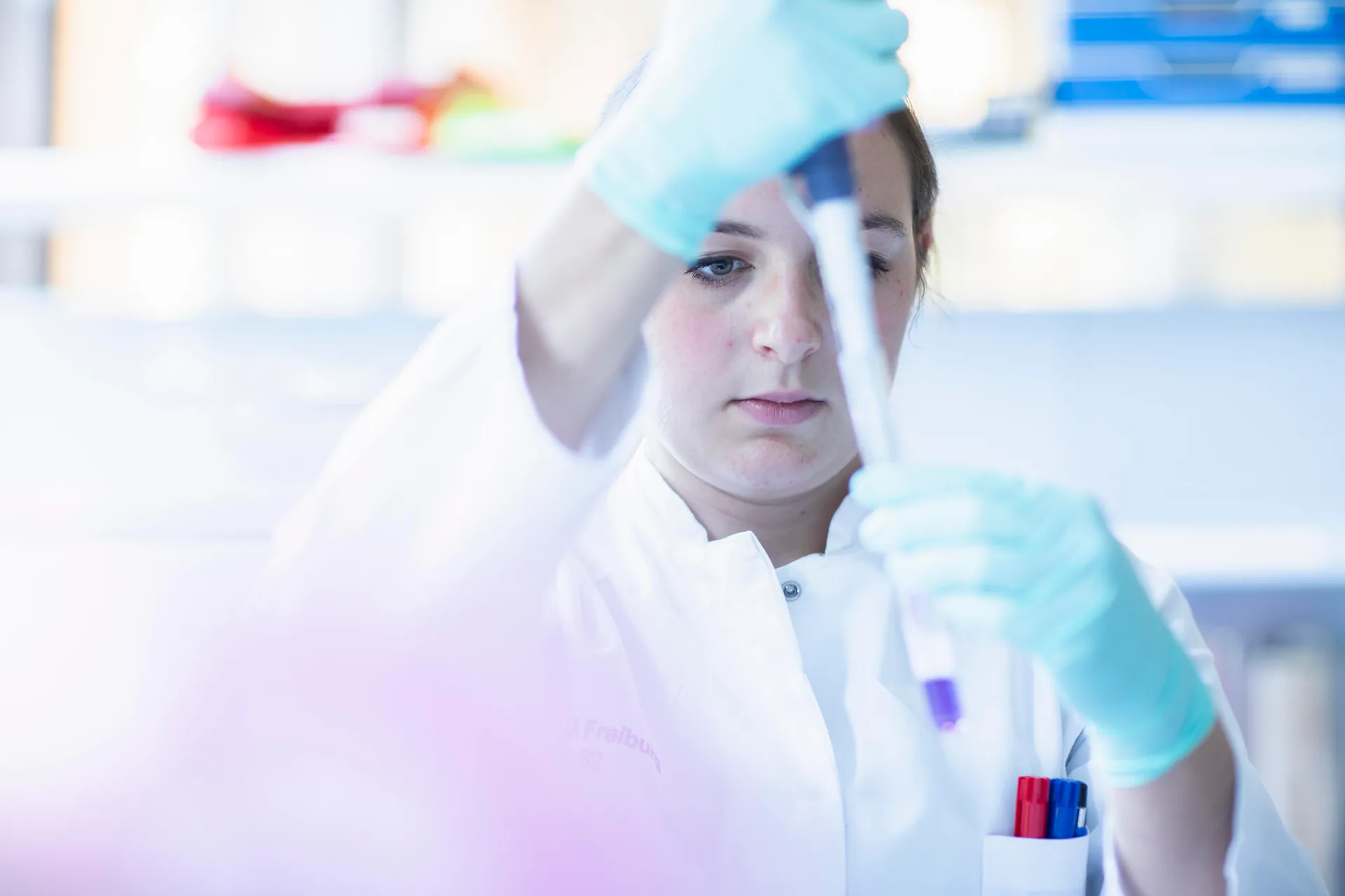 A lab technician works with a pipette and sample in a petri dish alongside lab equipment in Freiburg, Germany.