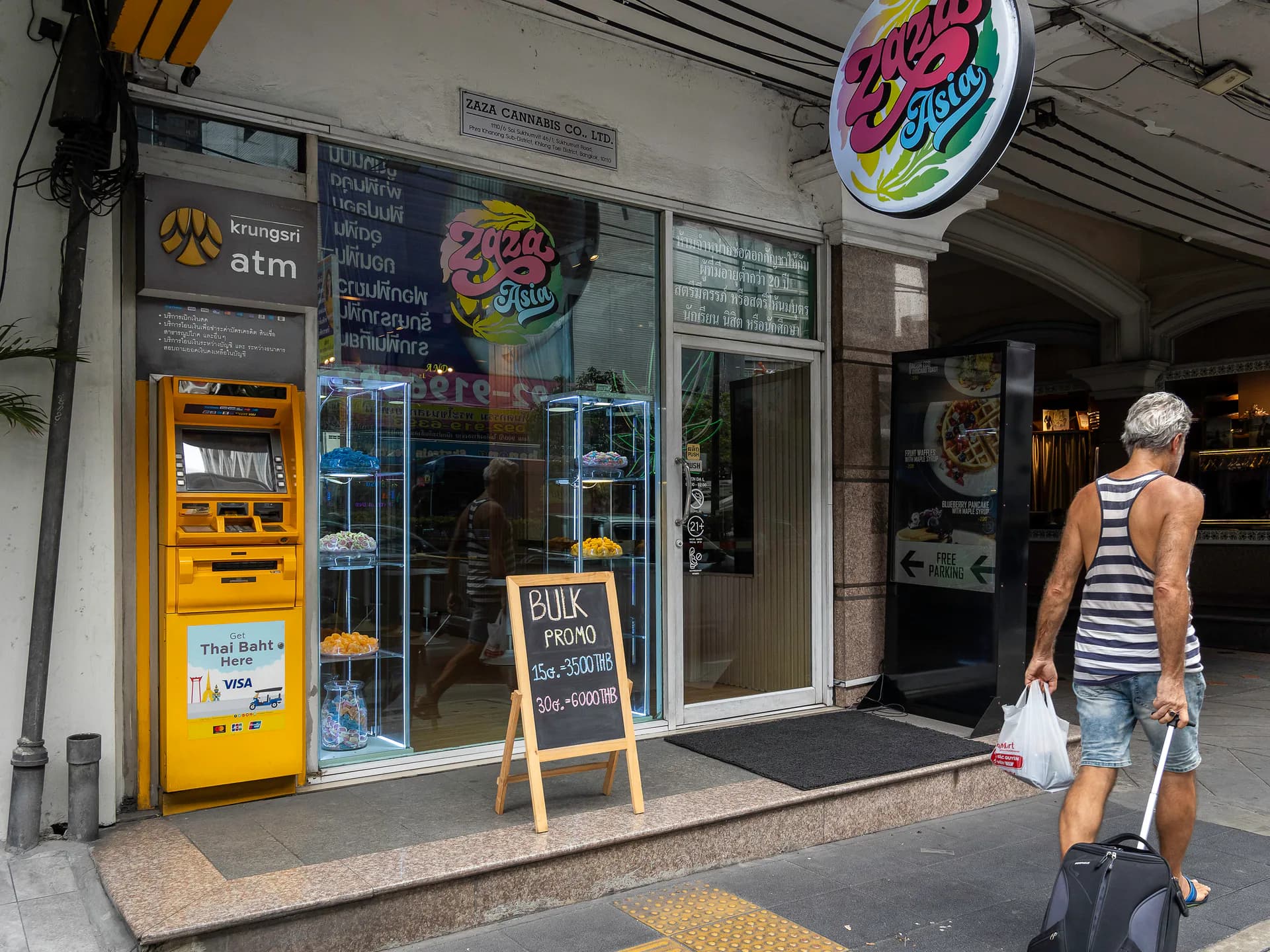 A tourist with his luggage passes in front of the ZaZa Asia cannabis dispensary, which advertises bulk cannabis promotions, near an ATM machine on Sukhumvit Road in Bangkok, Thailand, Friday, May 10, 2024. (Newscom)