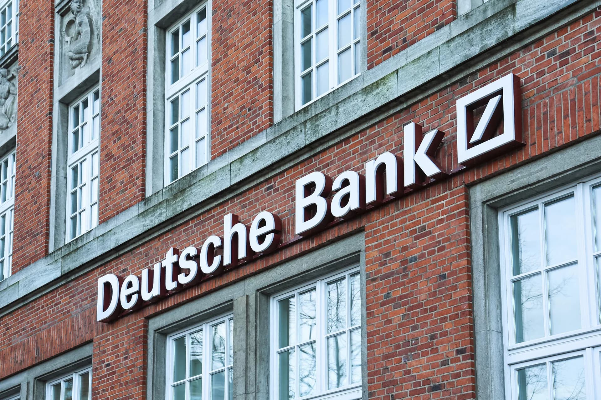 The Deutsche Bank logo and signage are displayed on the brick facade of a building branch.