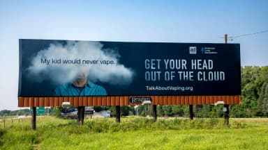 A billboard reading Get Your Head Out of the Cloud stands along a roadside, depicting a man with his head obscured by a cloud of vapor. | Michael Siluk/UCG/Universal Images Group/Newscom