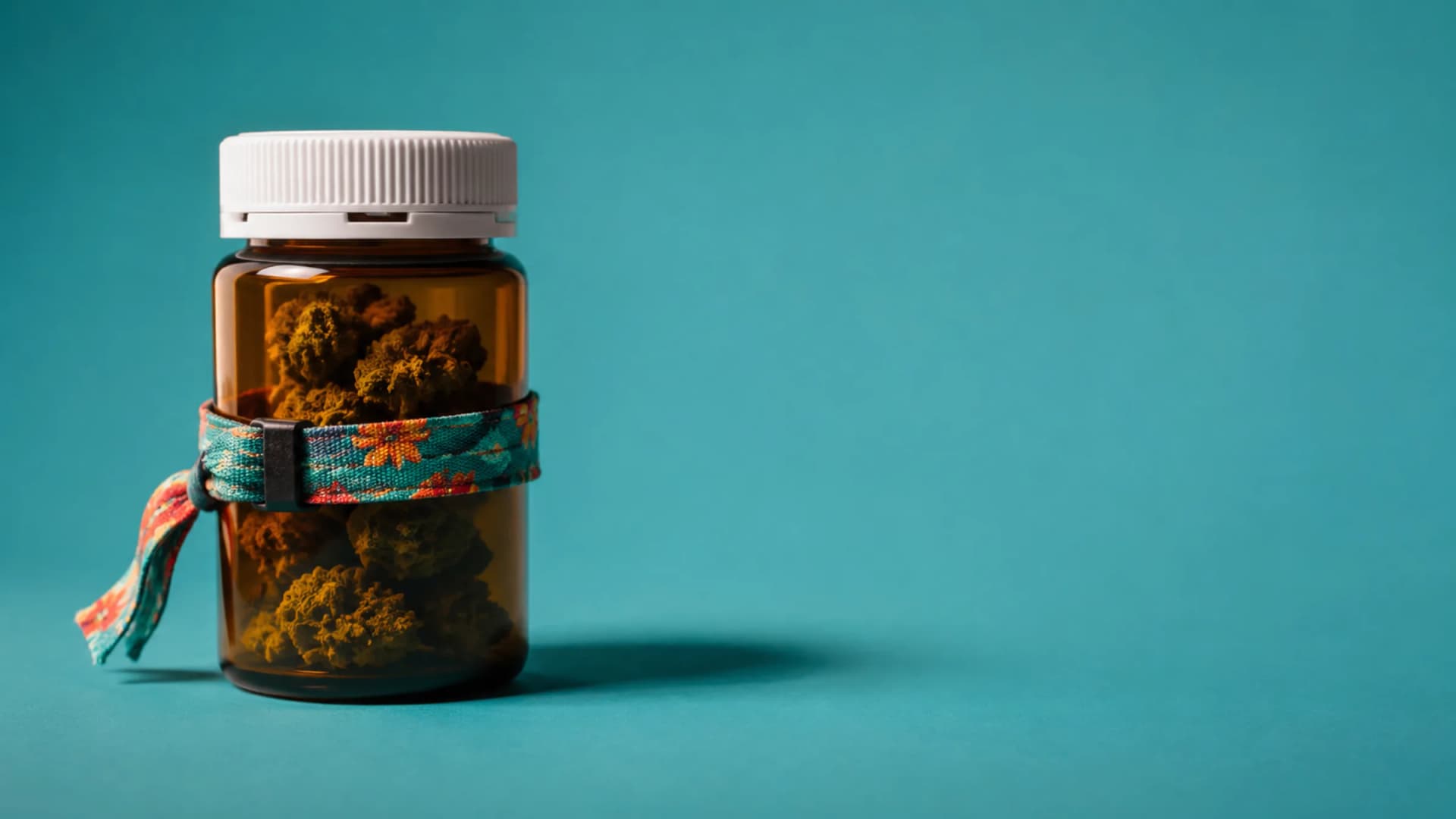 An amber pharmacy medicine bottle with a bright fabric festival wristband around it stands on a teal backdrop. (VapeExperts/AI)