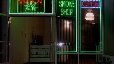 Neon signs reading Medical, Smoke Shop and Open glow in the barred windows of a medical marijuana shop at night. Wyoming has kept cannabis classified as Schedule I, rejecting a federal shift. (Laurie Avocado/Wikimedia Commons (CC BY 2.0))