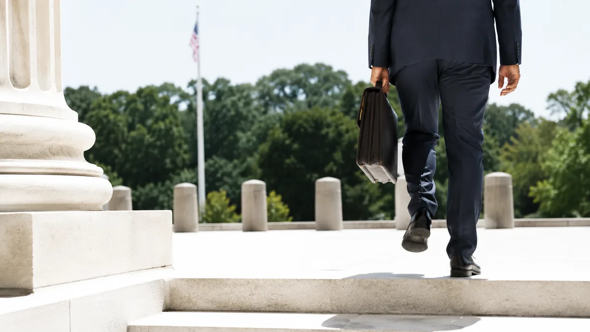 SHOT + MOMENT: The lower corner of an anonymous stone courthouse steps caught at the instant a lone figure in a summer-weight suit crests...
