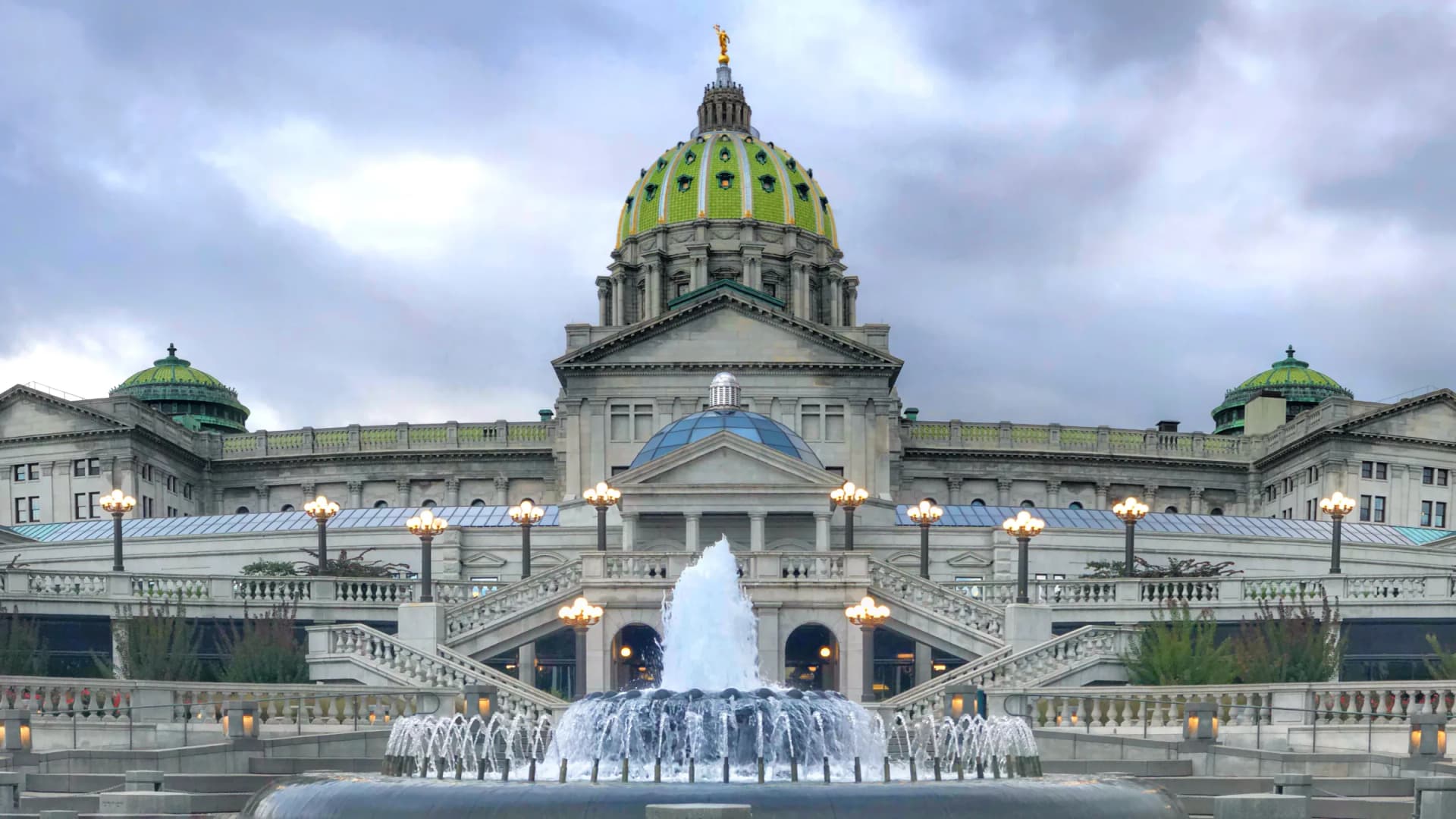 The Pennsylvania State Capitol in Harrisburg stands behind a fountain, its green tiled dome topped with a gold statue. Lawmakers there passed a state budget that again excludes legal cannabis. (Schindlerdigital/Wikimedia Commons (CC BY-SA 4.0))