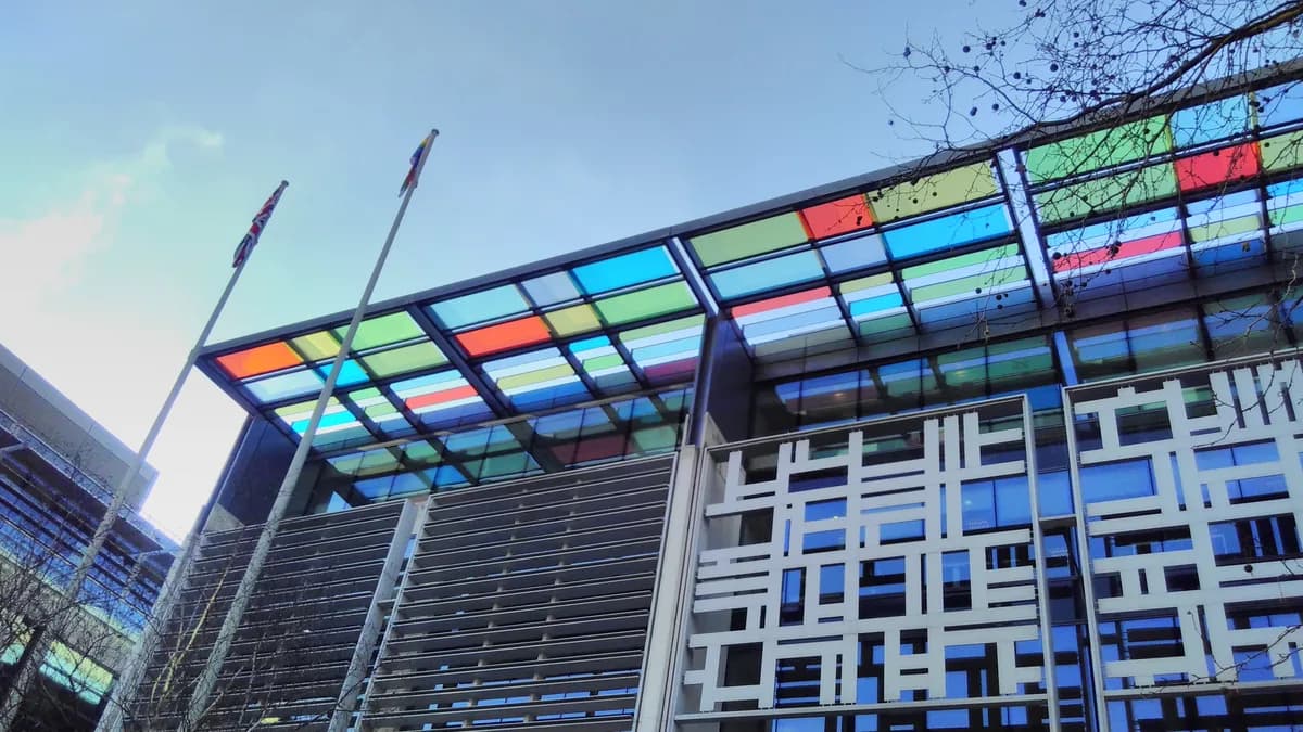 Low-angle view of the Home Office building in London, showing a colourful glass canopy, flagpoles and a patterned facade. | Charles Hutchins from London, United Kingdom/Wikimedia Commons (CC BY 2.0)