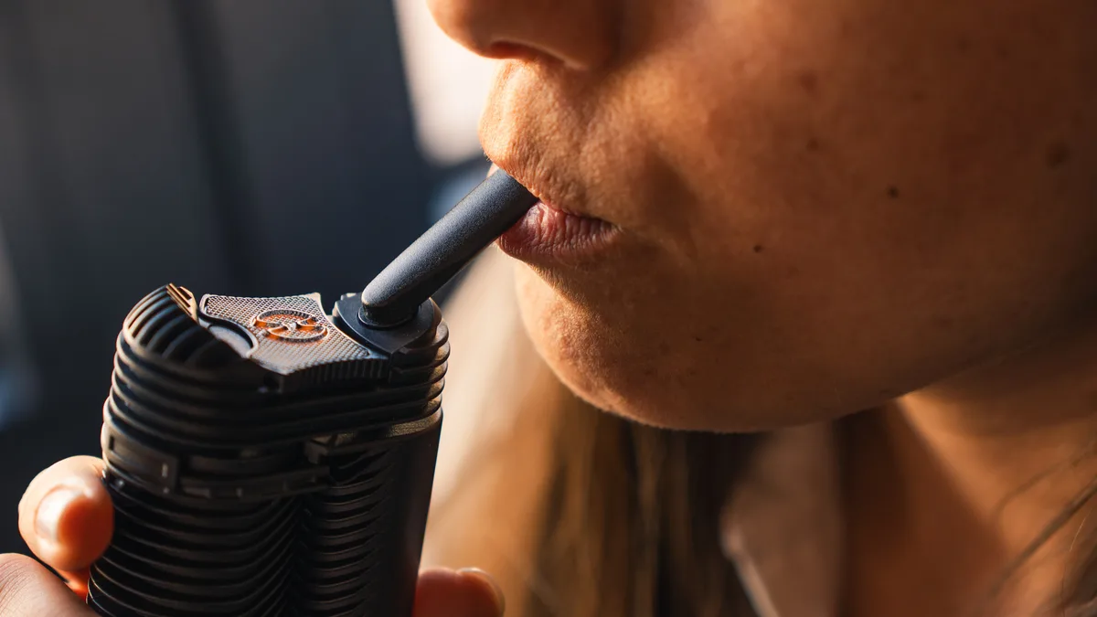 Close-up of a person holding a black Crafty+ vaporizer and drawing from its mouthpiece. | VapeExperts