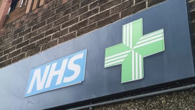 An NHS pharmacy sign with a green cross hangs on a brick wall in London on April 15, 2024. Private cannabis prescriptions in the UK have surged 134% as the NHS continues to deny most patients access. (imageBROKER/Zydrius Tartenis/Newscom)