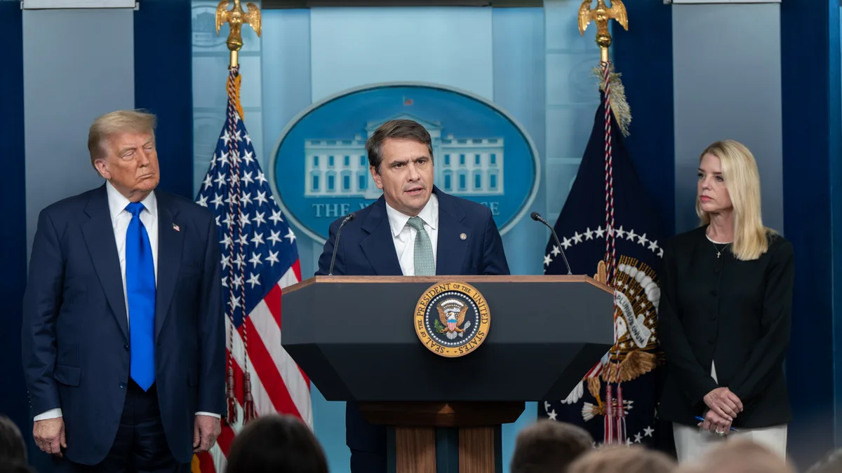 Todd Blanche speaks at a podium in the White House briefing room with Donald Trump and Pam Bondi standing on either side. | The White House/Wikimedia Commons (Public domain)