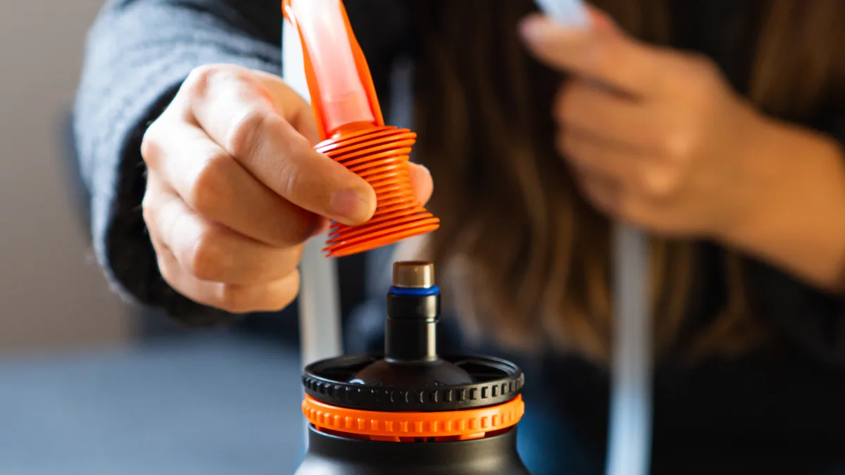 A person attaches an orange mouthpiece and tube to a black cone-shaped Volcano Hybrid vaporizer on a wooden table. | VapeExperts