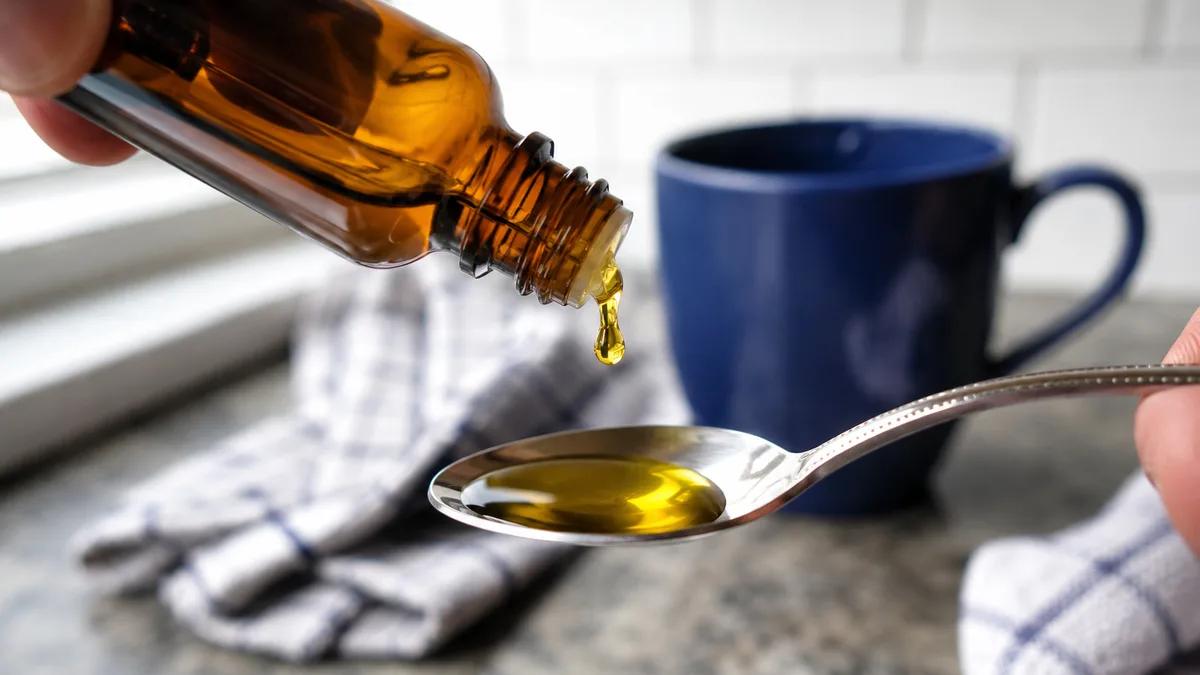 Amber dropper bottle with golden cannabis tincture oil being dispensed onto a spoon, kitchen counter background