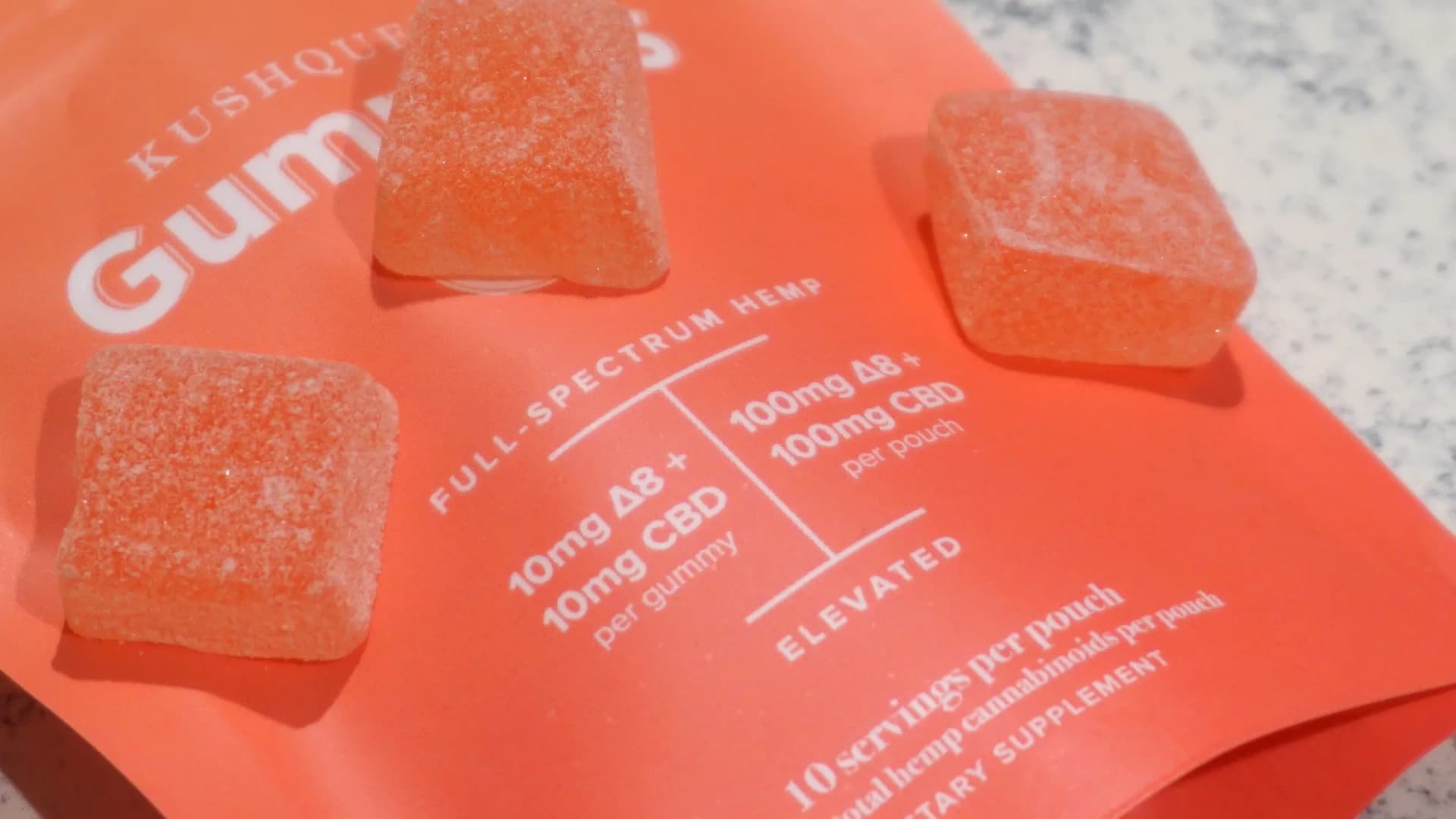 Sugar-coated Delta-8 THC gummies with CBD rest on an orange KushQueen pouch labeled full-spectrum hemp. Texas has banned Delta-8 products, making possession a felony. (elsaolofsson/Wikimedia Commons (CC BY 2.0))