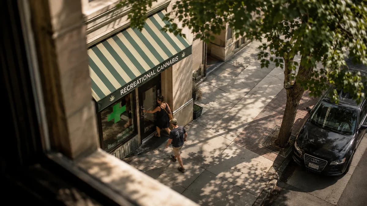 SHOT + MOMENT: From a second-story window across a narrow street, looking steeply down onto the striped awning of a small recreational...