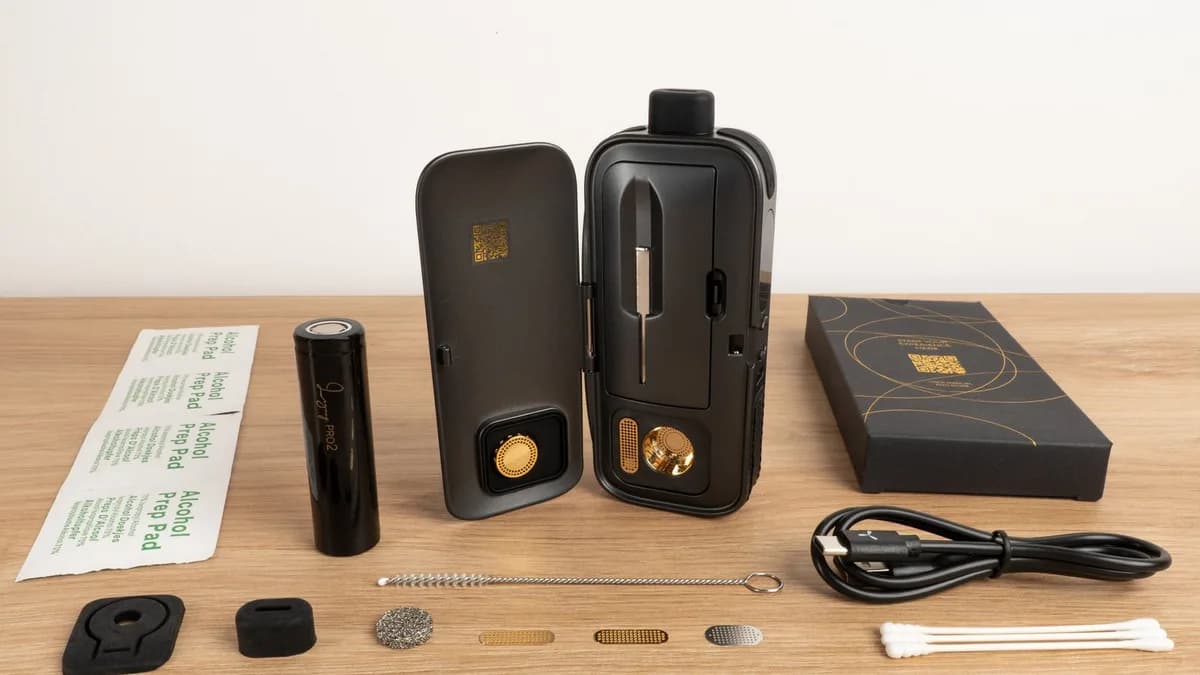A black AirVape Legacy Pro 2 vaporizer with its door open, laid out on a wooden table with a battery, screens, brush, cable and swabs. | VapeExperts