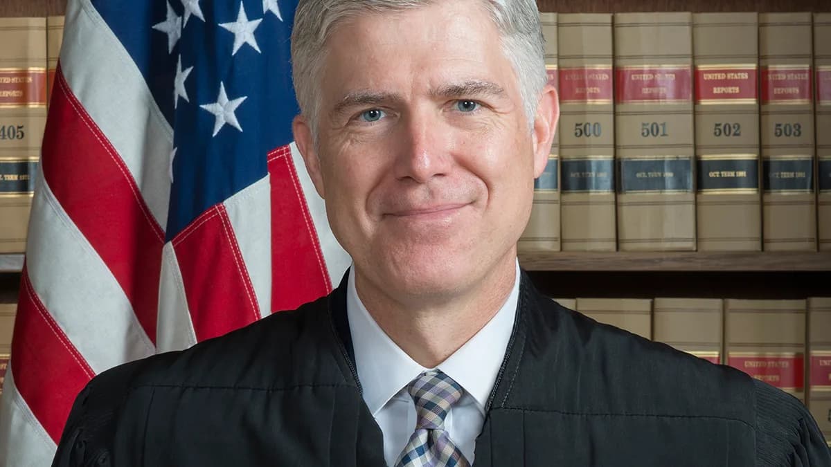 A smiling man with gray hair in a black judicial robe and checked tie stands in front of an American flag and shelves of legal volumes. | Franz Jantzen, Collection of the Supreme Court of the United States/Wikimedia Commons (Public domain)