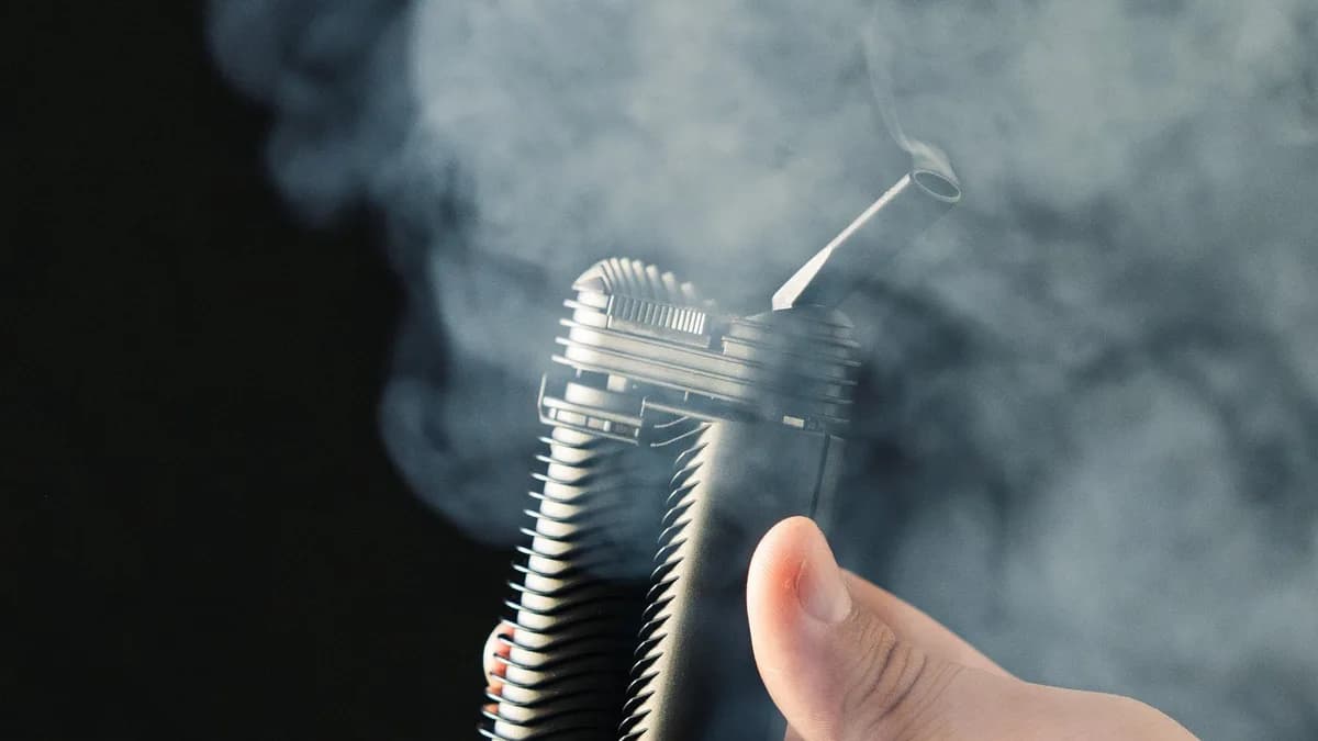 A hand holds a black Storz & Bickel Crafty+ vaporizer with vapor rising from its mouthpiece against a dark background. | VapeExperts