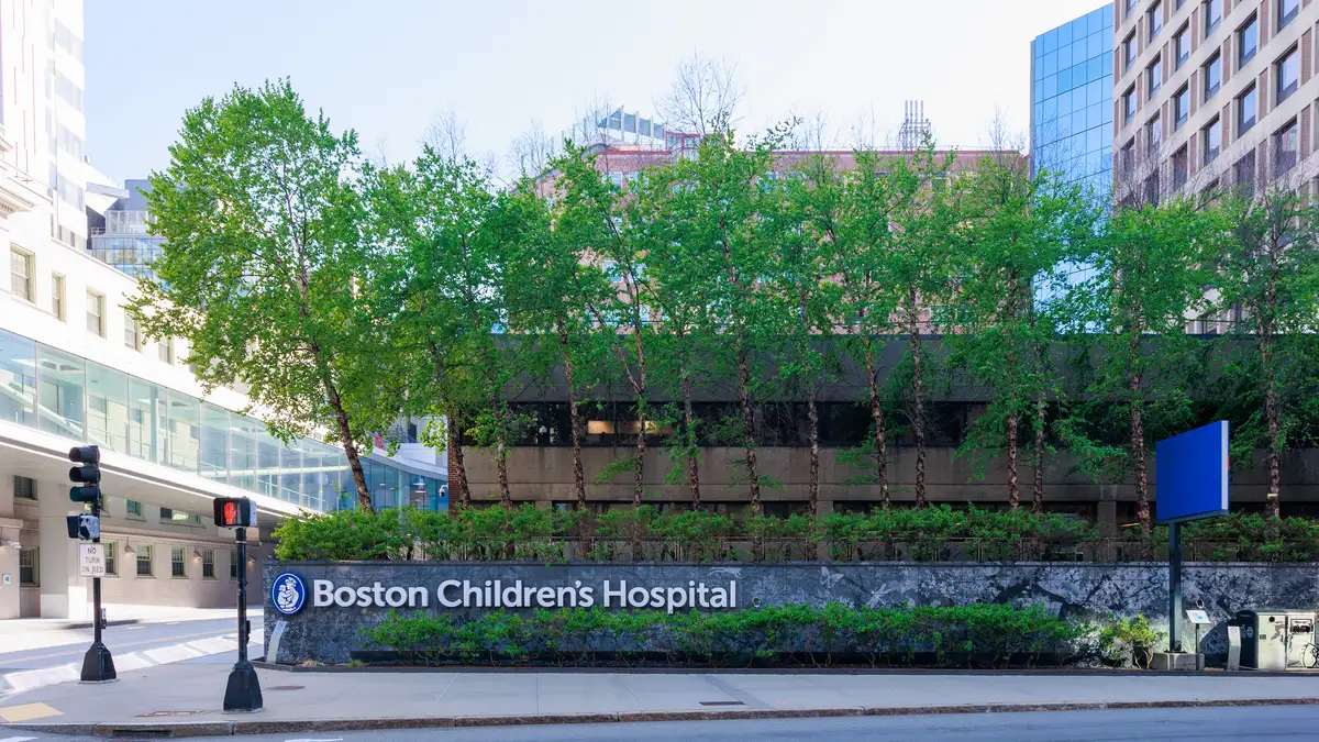 Street view of the Boston Children's Hospital sign on a low stone wall along Longwood Avenue, with trees and hospital buildings behind it. | Kenneth C. Zirkel/Wikimedia Commons (CC BY-SA 4.0)